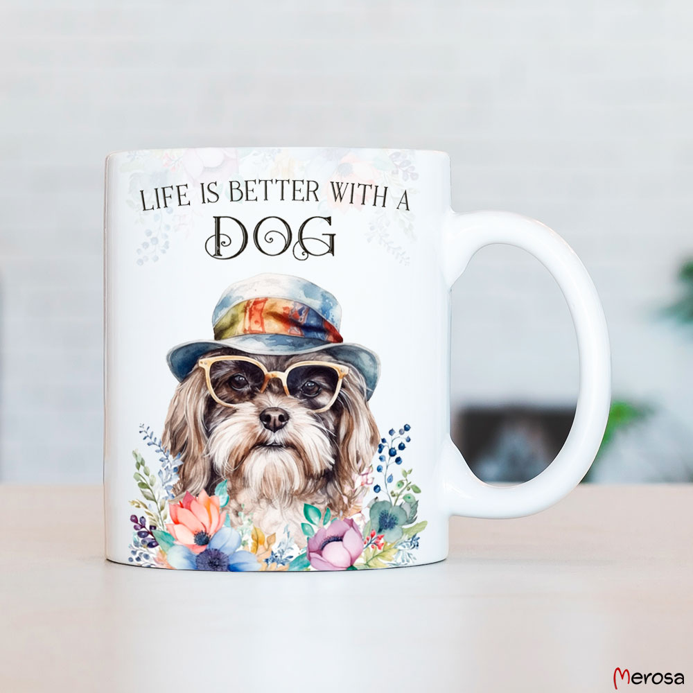 eine weiße Tasse aus Keramik, die beidseitig bedruckt ist mit einem Havaneser mit Brille und Hut, im fröhlich bunten Watercolor-Stil, verziert mit einer bunten Blumenranke am oberen und unteren Rand und dem englischen Spruch „Life is better with a Dog“